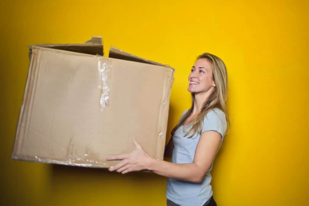 femme qui porte un carton devant un mur jaune